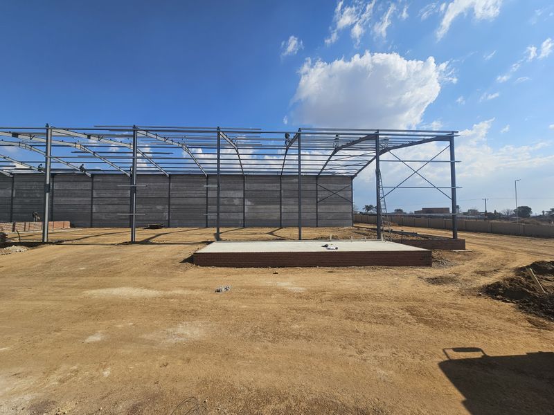 Industrial property under construction featuring a steel portal frame structure and a concrete foundation slab on an unpaved site.