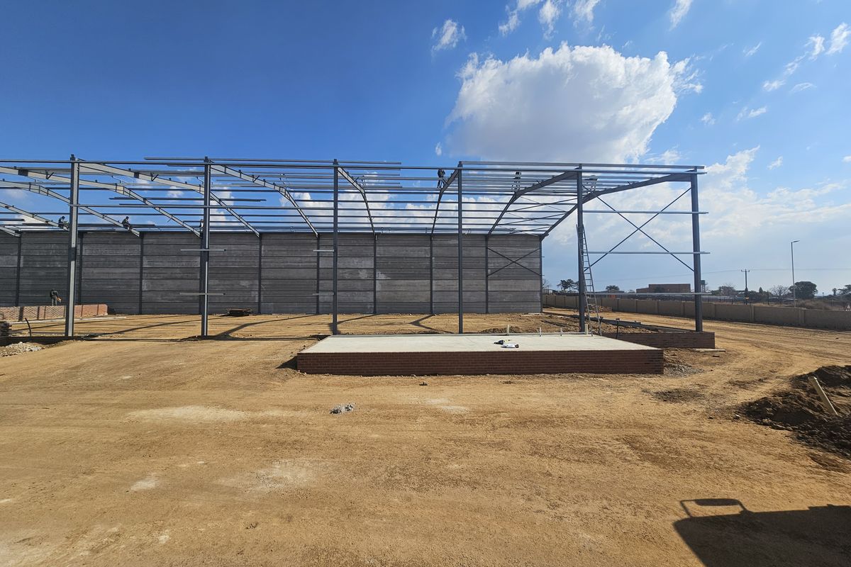 Industrial property under construction featuring a steel portal frame structure and a concrete foundation slab on an unpaved site.