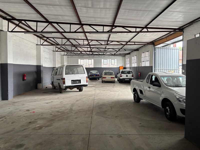 Spacious industrial garage featuring exposed steel roof trusses, concrete flooring, and large multi-pane windows, suitable for vehicle storage or workshop use.
