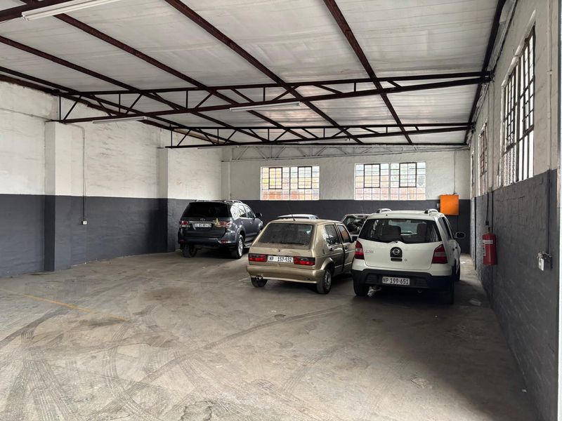 Spacious industrial garage featuring exposed steel roof trusses, concrete flooring, and large metal-framed windows, suitable for vehicle storage or workshop use.