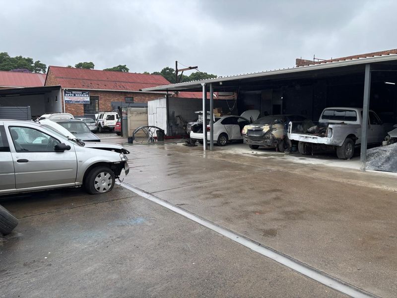 Industrial workshop area featuring a large concrete hardstand and a steel-framed covered workspace suitable for automotive repair operations.