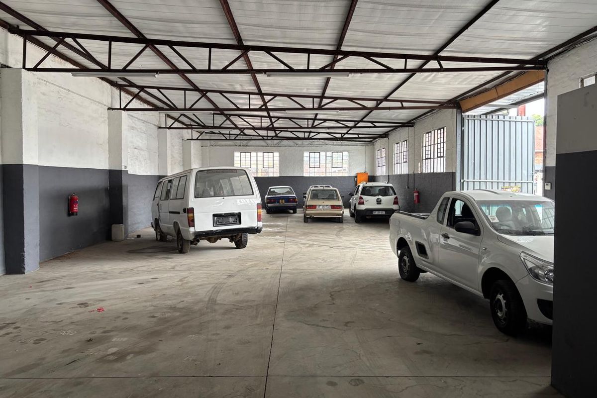 Spacious industrial garage featuring exposed steel roof trusses, concrete flooring, and large multi-pane windows, suitable for vehicle storage or workshop use.