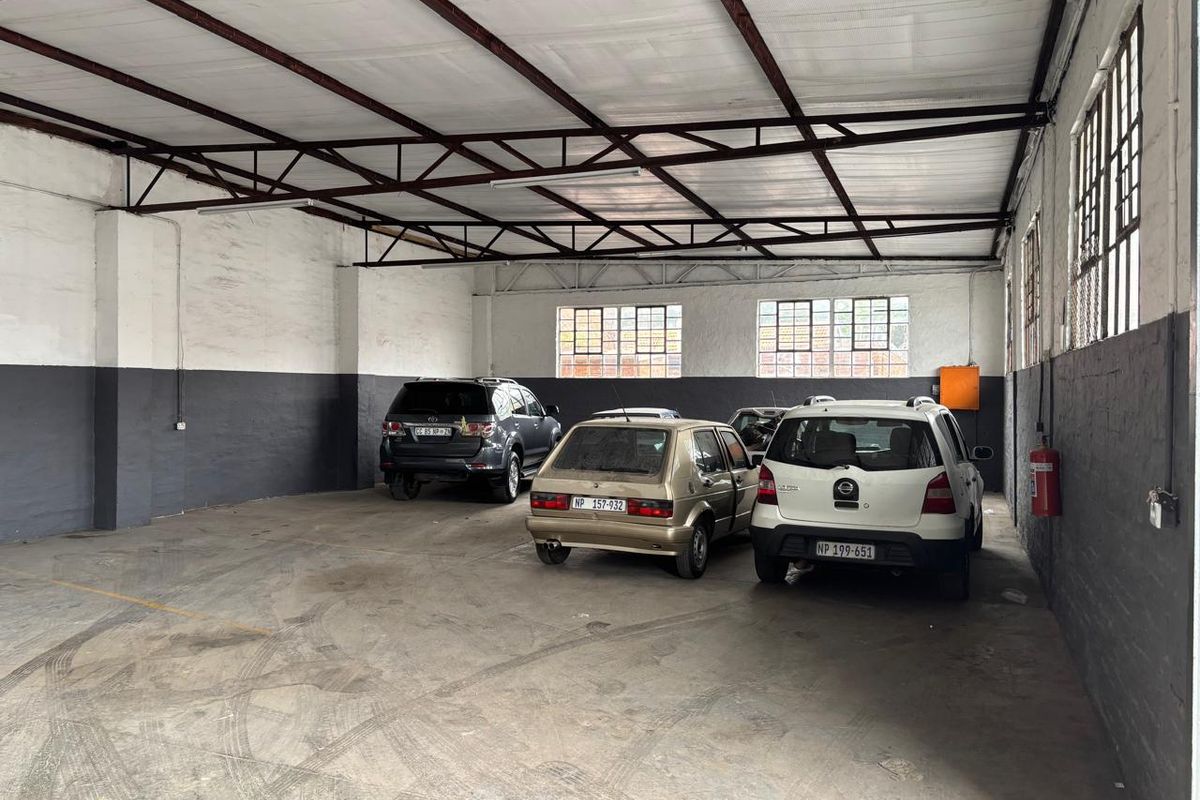 Spacious industrial garage featuring exposed steel roof trusses, concrete flooring, and large metal-framed windows, suitable for vehicle storage or workshop use.