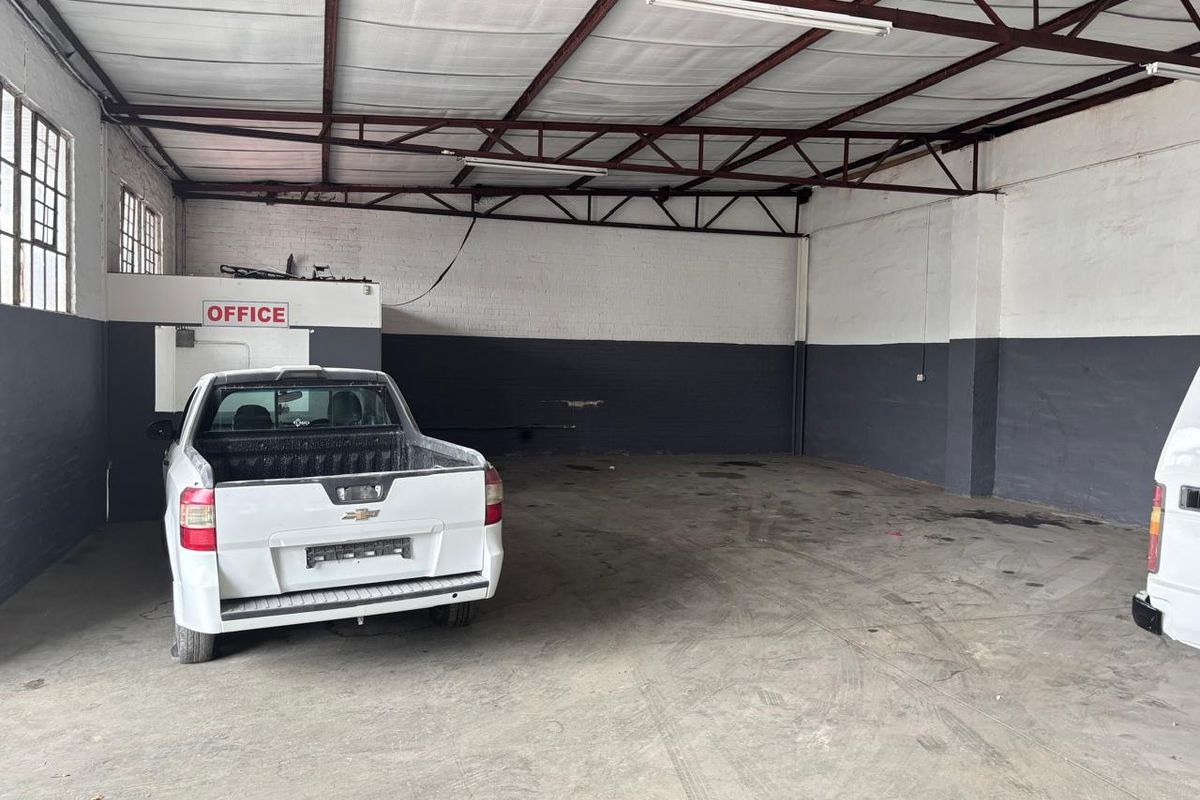 Spacious industrial garage or warehouse area featuring exposed steel roof trusses, concrete flooring, and a dedicated enclosed office space.