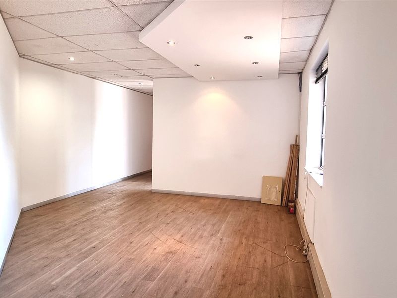 A bright, empty office space featuring laminate flooring, a suspended ceiling with recessed lighting, and a side window.