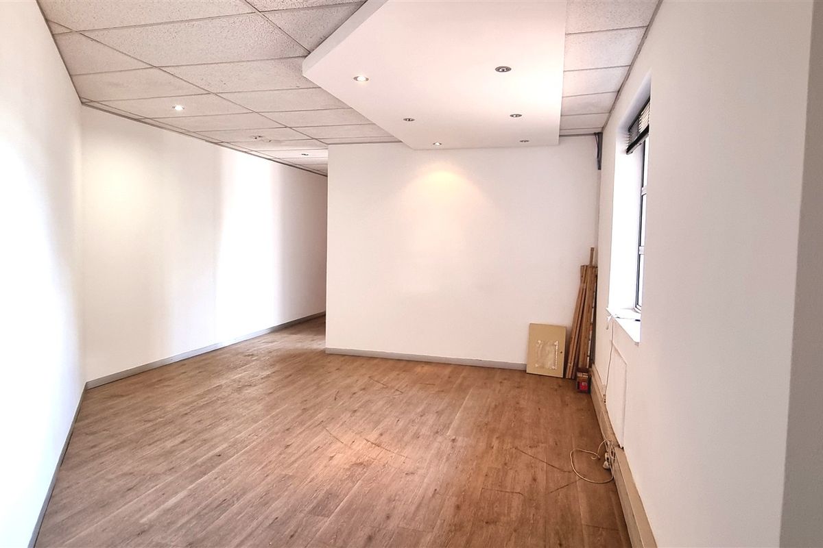 A bright, empty office space featuring laminate flooring, a suspended ceiling with recessed lighting, and a side window.