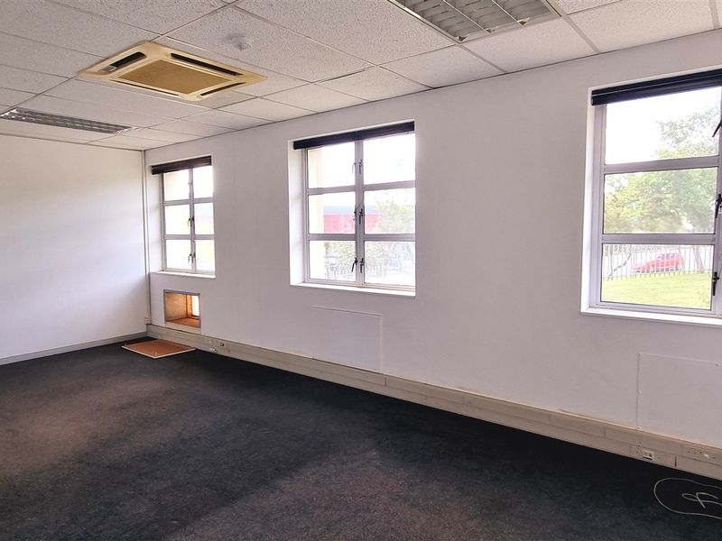 An empty office space featuring a suspended ceiling with integrated air conditioning, large aluminium windows, and carpeted flooring.
