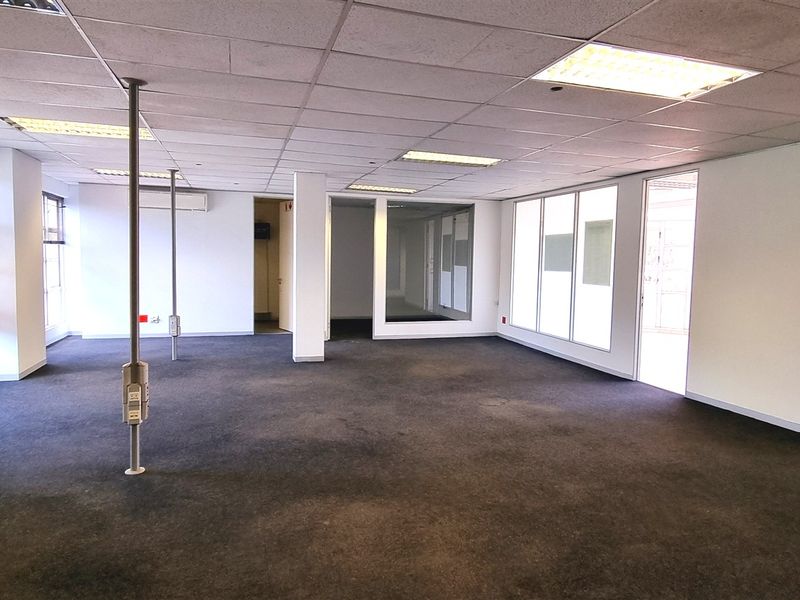 Spacious open-plan office area featuring large windows, suspended ceilings with recessed lighting, and a private glass-partitioned office space.