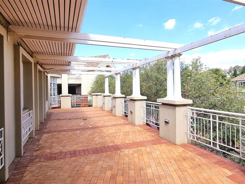 Spacious outdoor balcony featuring brick paving, a pergola structure with columns, and metal railings, offering a functional exterior space for the office property.
