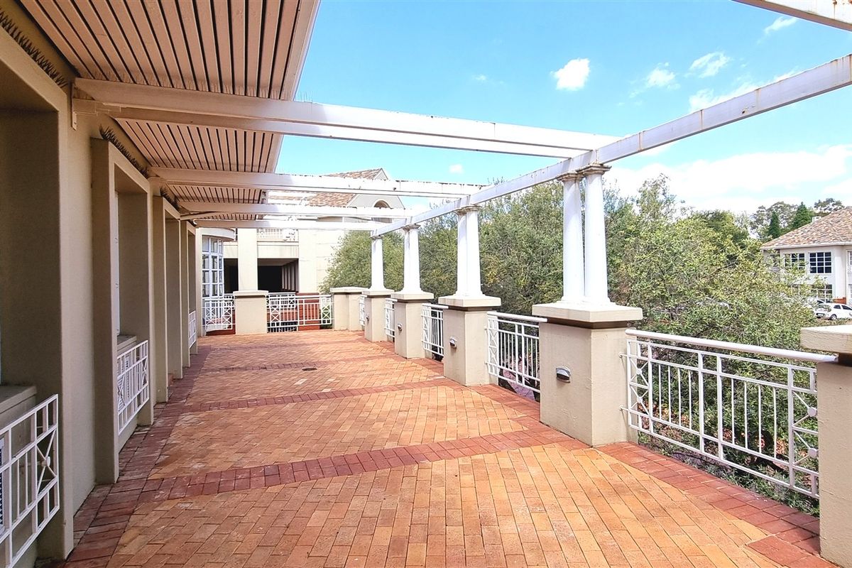 Spacious outdoor balcony featuring brick paving, a pergola structure with columns, and metal railings, offering a functional exterior space for the office property.