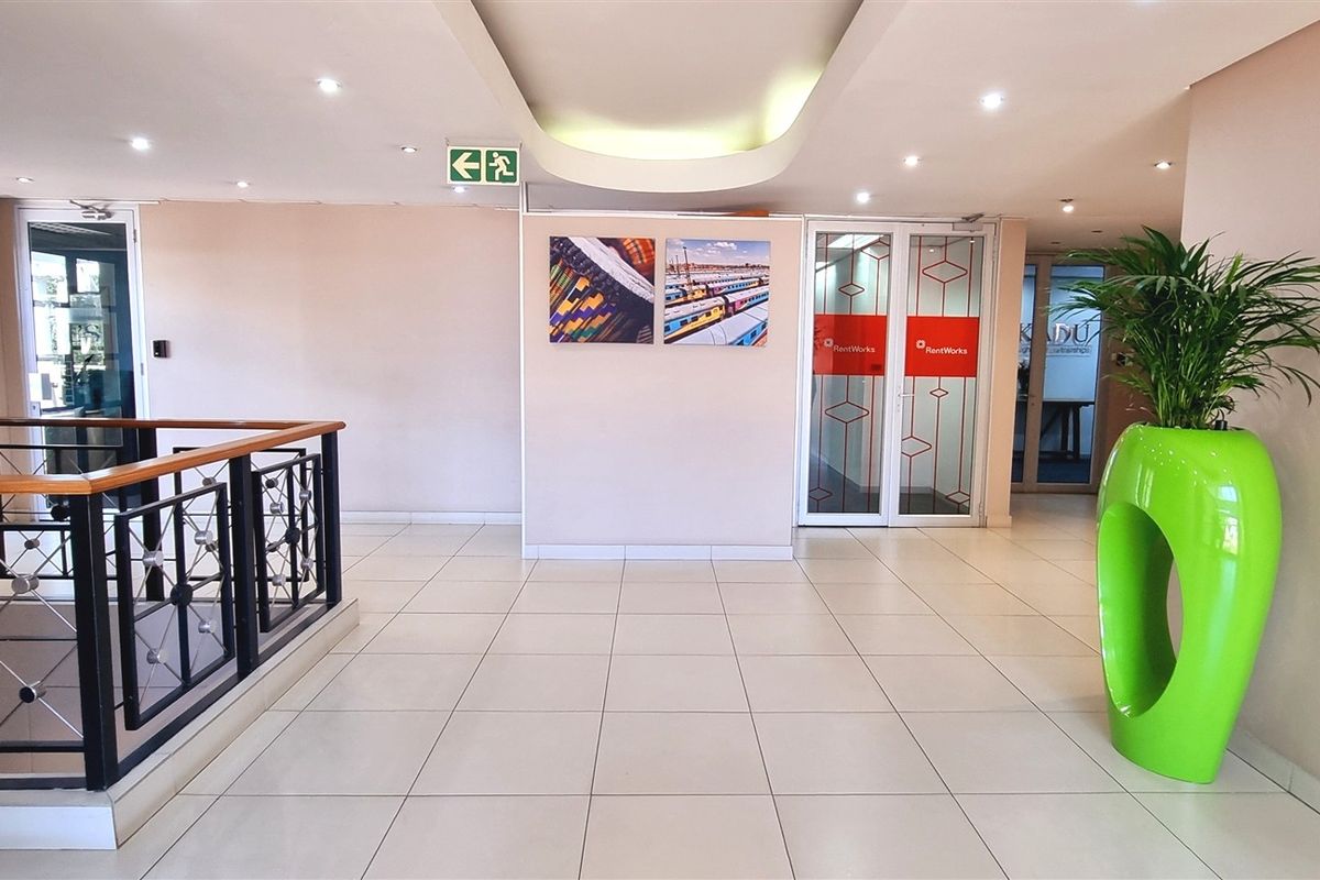 A bright and spacious office building entrance lobby featuring tiled flooring, recessed ceiling lighting, and a modern metal balustrade overlooking the stairwell.