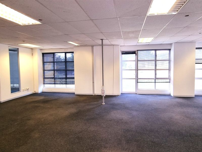 A spacious, open-plan office area featuring suspended ceilings, recessed lighting, and large windows providing ample natural light.