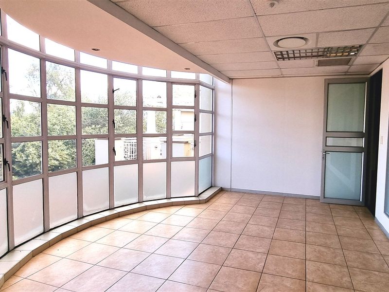 A bright, empty office space featuring large curved windows, tiled flooring, and a suspended ceiling with integrated lighting.