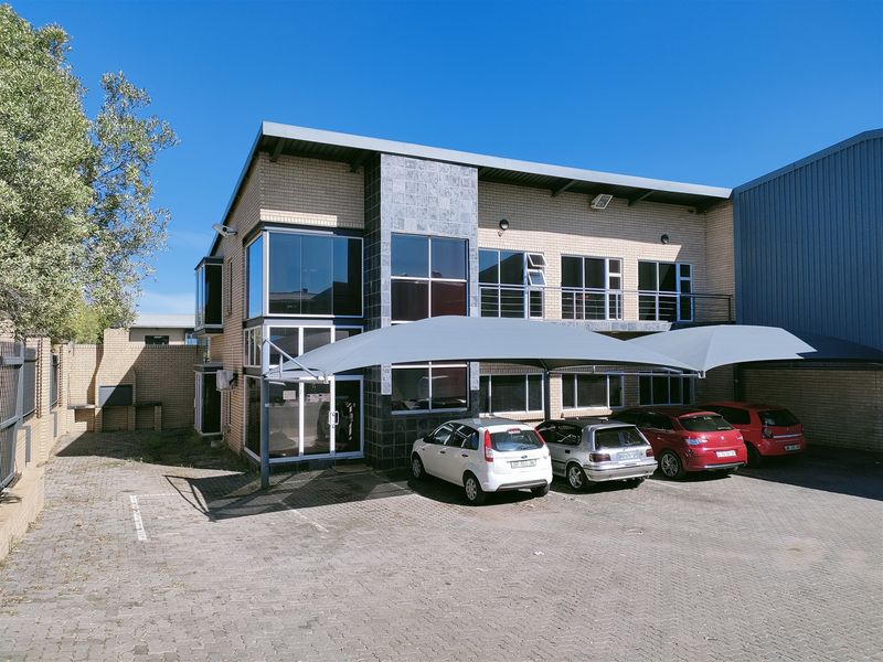 Modern industrial office building featuring a brick and stone facade, large aluminium windows, and a paved parking area with shade sail carports.