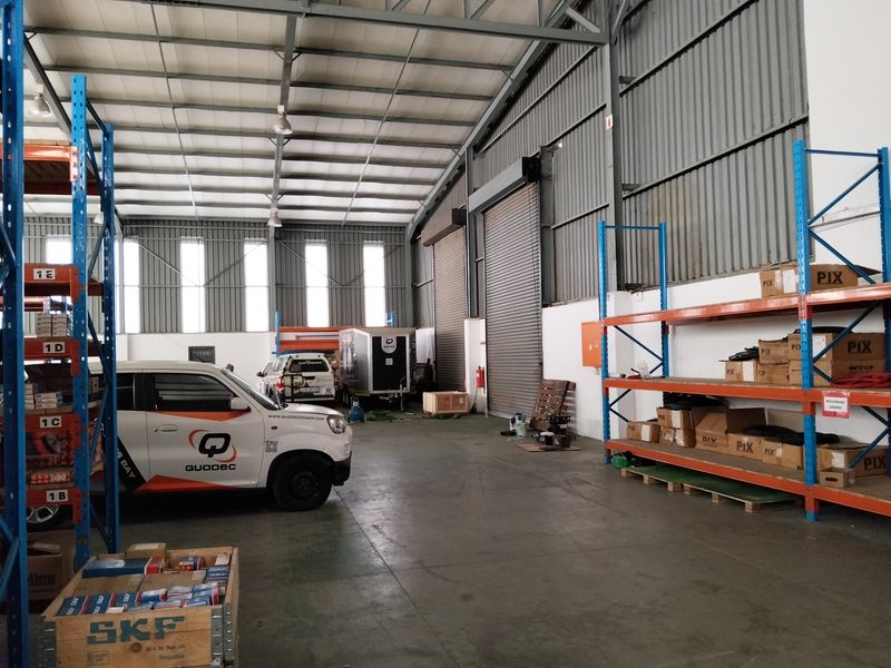 Spacious industrial warehouse unit featuring high ceilings with exposed steel trusses, concrete flooring, and heavy-duty racking systems.