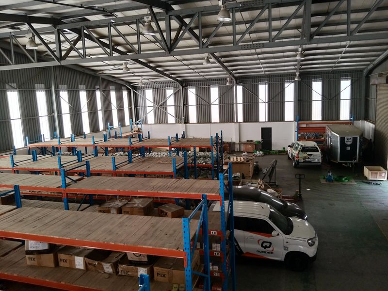 Spacious industrial warehouse featuring a steel portal frame, high-bay lighting, concrete flooring, and extensive built-in racking systems suitable for storage or manufacturing operations.