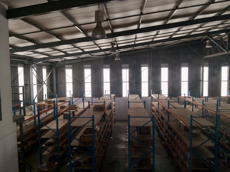 Spacious industrial warehouse interior featuring high ceilings, exposed steel structural elements, and extensive fixed metal racking systems for storage.