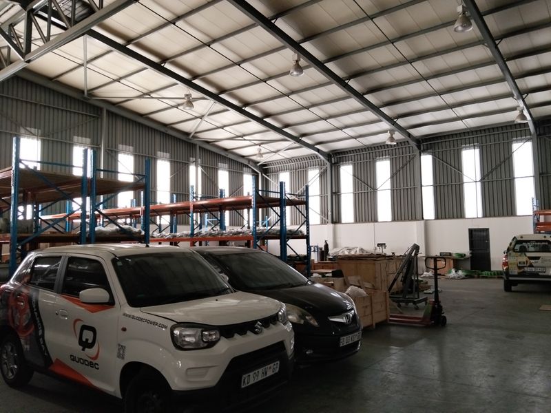 Spacious industrial warehouse featuring high ceilings with exposed steel trusses, concrete flooring, and integrated steel racking systems for storage.