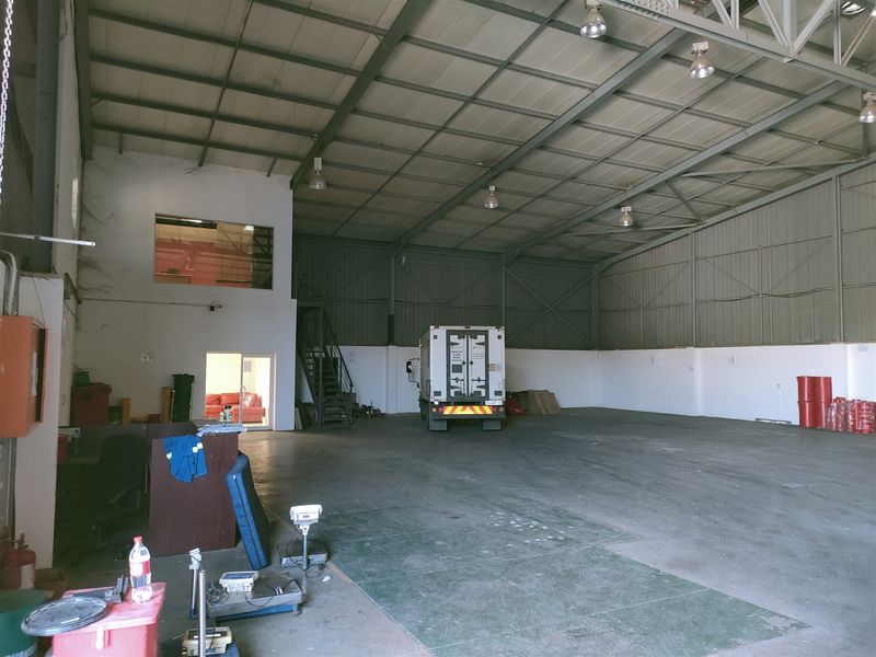 Spacious industrial warehouse featuring high ceilings with exposed steel trusses, concrete flooring, and a mezzanine level, suitable for storage or manufacturing operations.