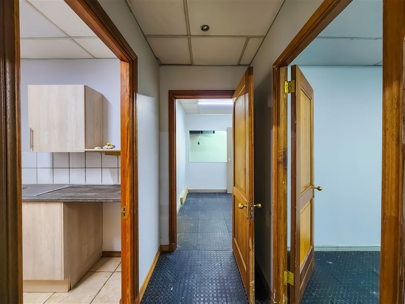 A functional office hallway connecting multiple rooms, featuring durable rubber flooring, timber door frames, and access to a small kitchenette area.