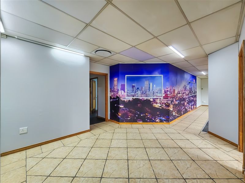 A spacious office hallway featuring tiled flooring, a suspended ceiling with integrated lighting, and a decorative wall mural.