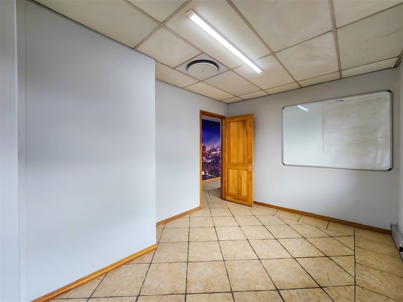 A functional office space featuring tiled flooring, a suspended ceiling with integrated lighting, and a wall-mounted whiteboard.