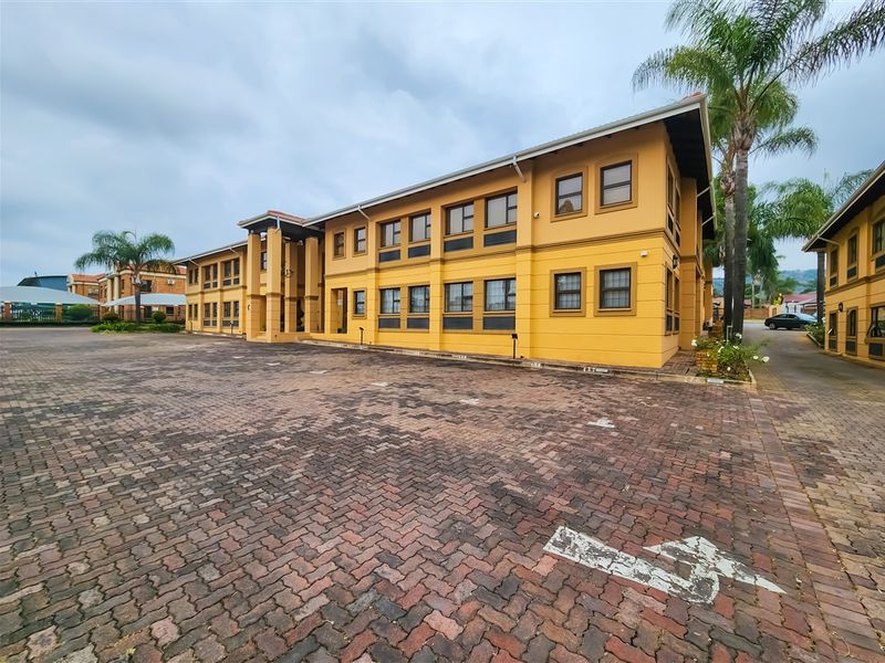 A multi-story office building exterior featuring a large paved parking area and a yellow facade with multiple window bays.