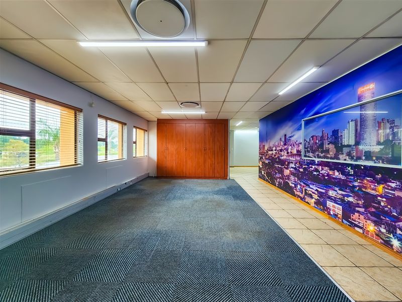 Spacious open-plan office area featuring suspended ceilings, built-in storage cabinetry, carpeted flooring, and large windows with venetian blinds.