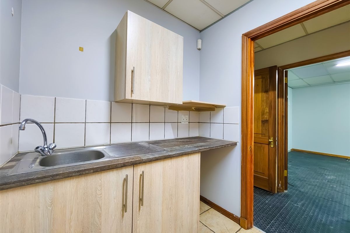 A compact office kitchenette featuring light wood-finish cabinetry, a stainless steel sink, tiled backsplash, and a durable laminate countertop.