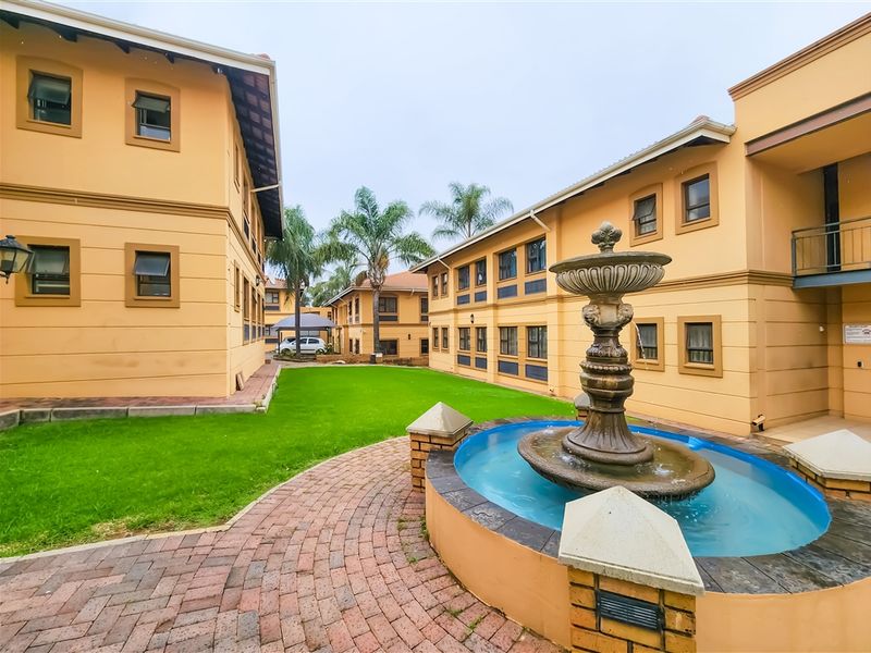 A well-maintained courtyard area featuring a central decorative fountain, brick paved pathways, and manicured lawn between office building wings.