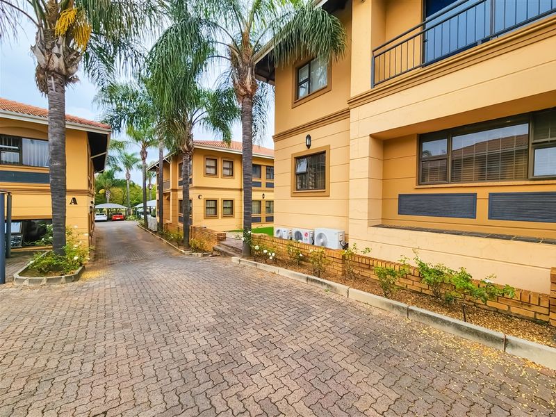 Exterior view of a multi-story office complex featuring paved driveways, landscaped palm trees, and well-maintained building facades with external air conditioning units.