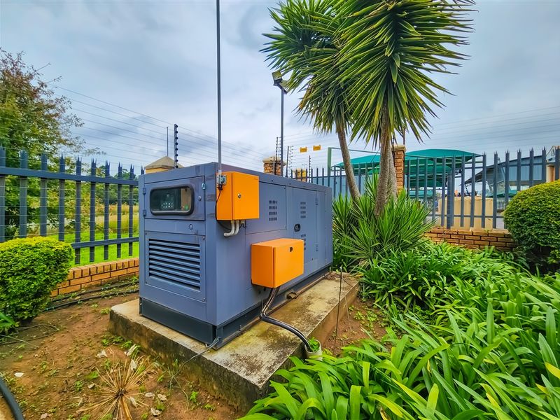 Outdoor utility area featuring a backup generator mounted on a concrete plinth, secured within a fenced perimeter.