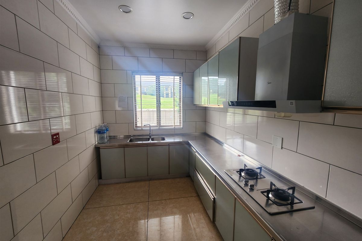 A functional kitchen featuring stainless steel countertops, a built-in gas hob, an extractor fan, double sink, and full-height wall tiling.