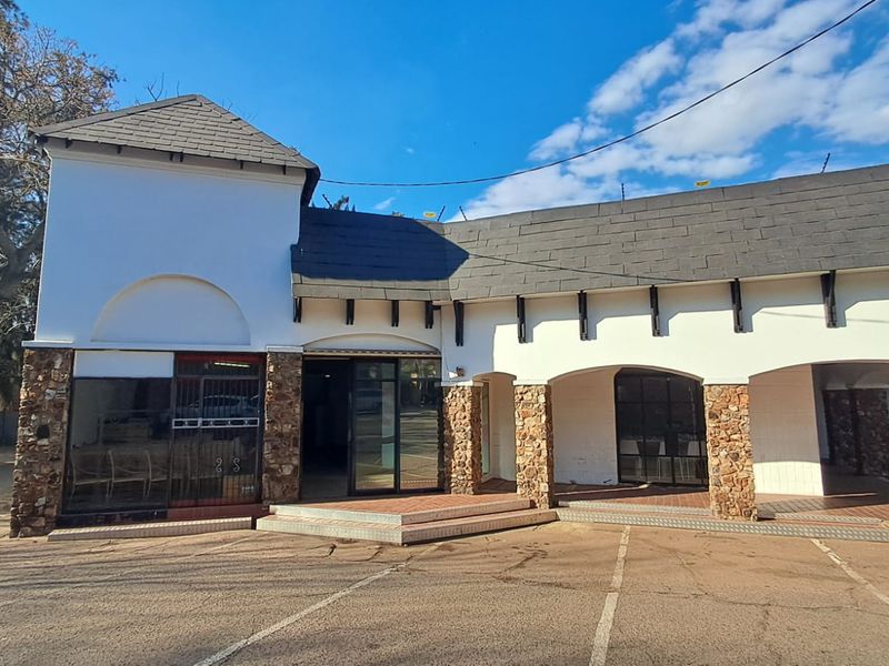 Front elevation of a retail property featuring stone cladding, arched architectural details, glass storefront entrances, and an adjacent paved parking area.