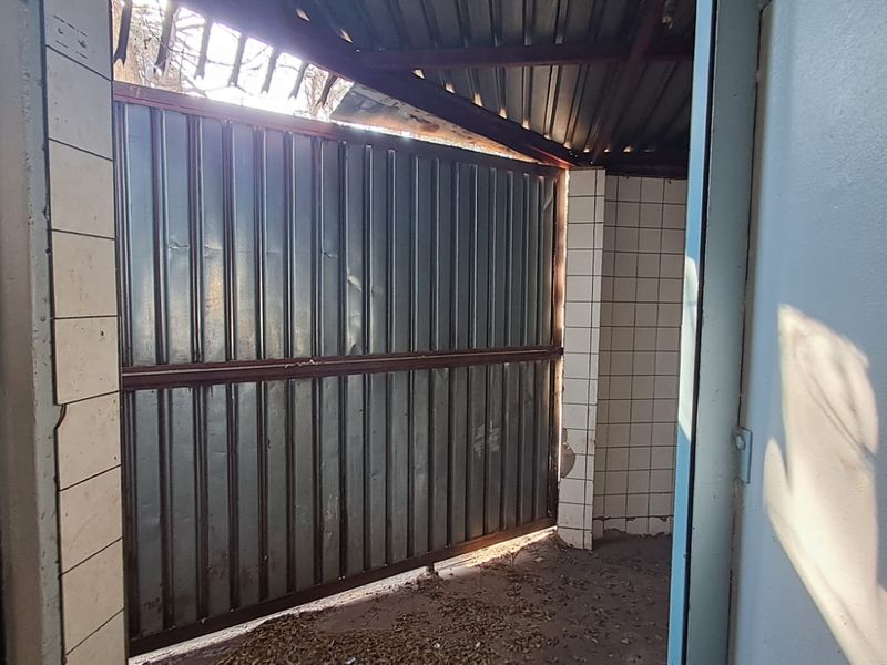 A utilitarian service area featuring tiled walls and a corrugated metal gate, currently showing significant signs of wear and structural damage.