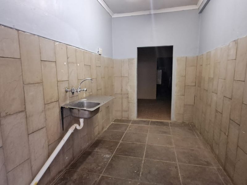 A functional scullery or utility area featuring a stainless steel sink, tiled walls, and tiled flooring, suitable for prep or wash-up tasks.
