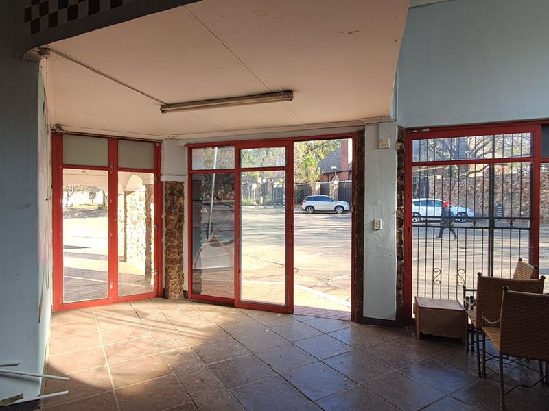 Entrance area featuring tiled flooring, red-framed glass doors, and security gates, providing direct access to the exterior parking area.