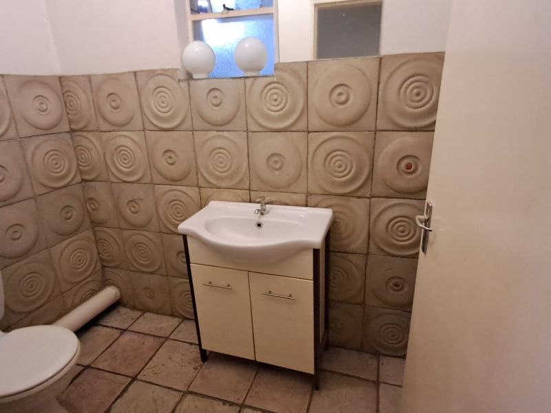 A compact bathroom featuring a vanity basin, toilet, and distinctive textured wall tiles, currently presenting in a dated condition.