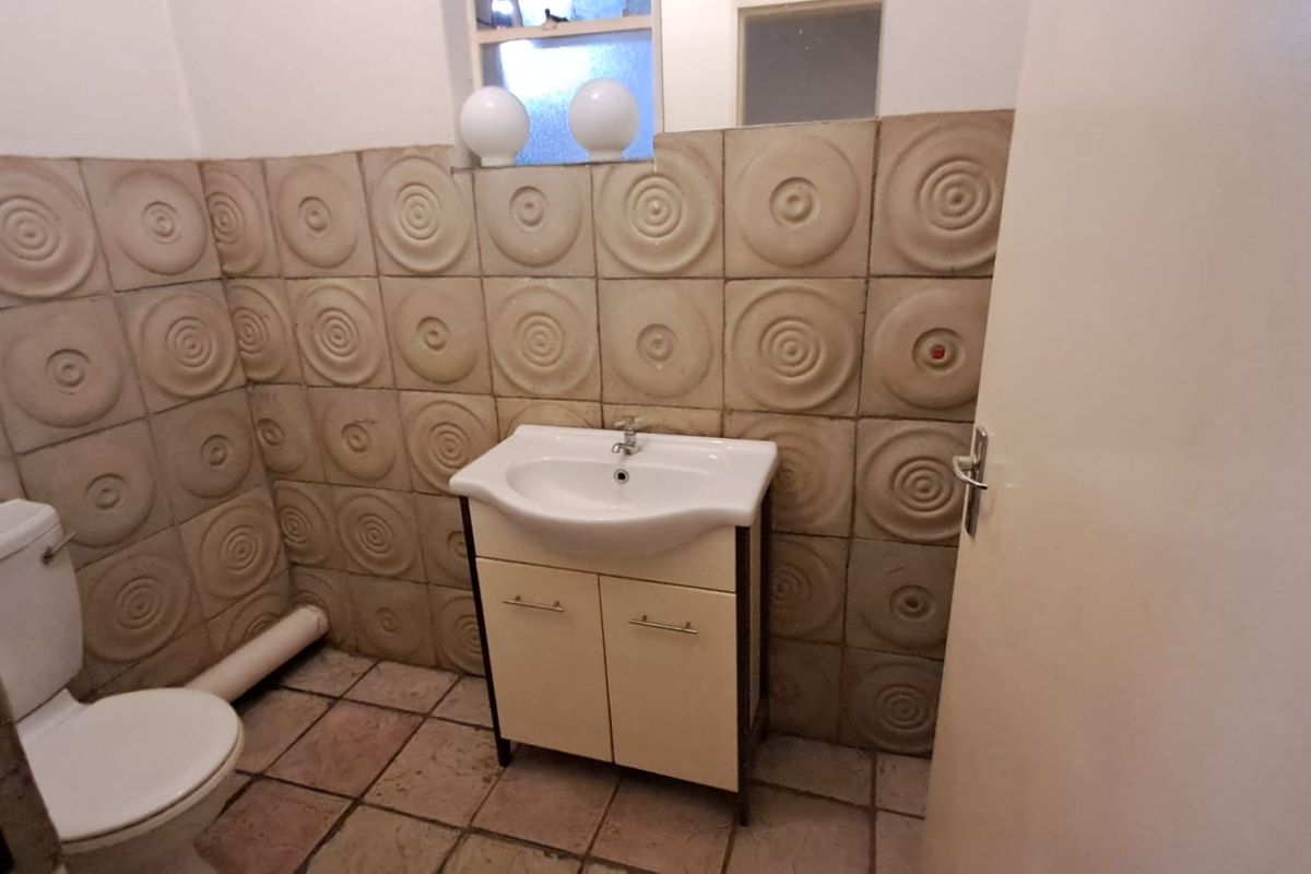 A compact bathroom featuring a vanity basin, toilet, and distinctive textured wall tiles, currently presenting in a dated condition.