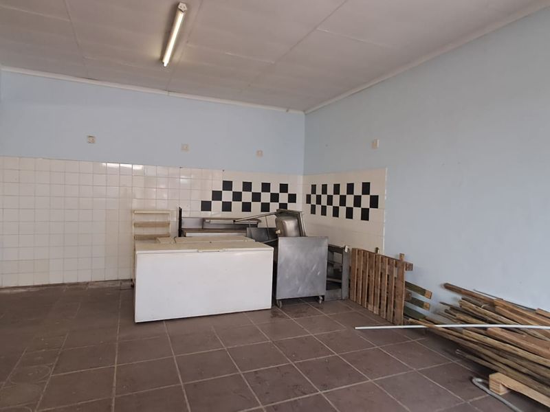 A vacant commercial kitchen space featuring tiled flooring, a tiled splashback, and basic utility lighting, suitable for a variety of retail or food service uses.
