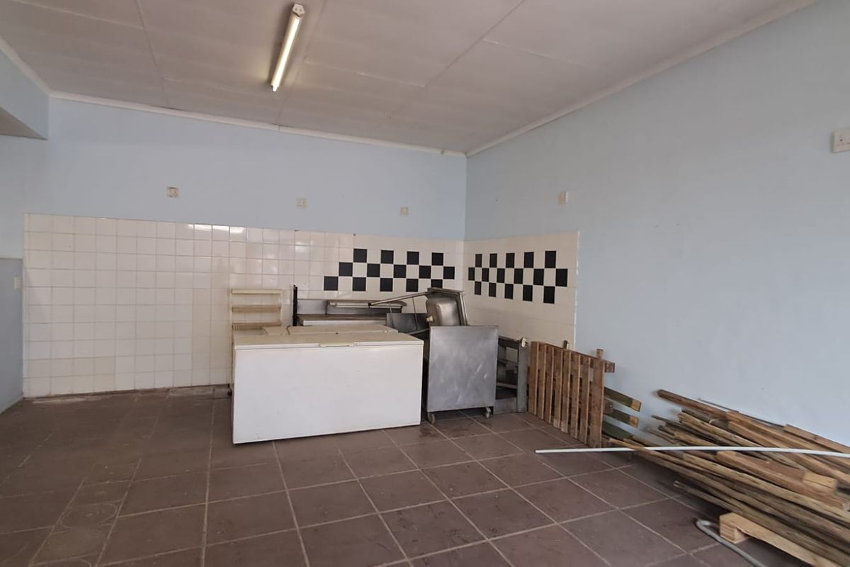 A vacant commercial kitchen space featuring tiled flooring, a tiled splashback, and basic utility lighting, suitable for a variety of retail or food service uses.