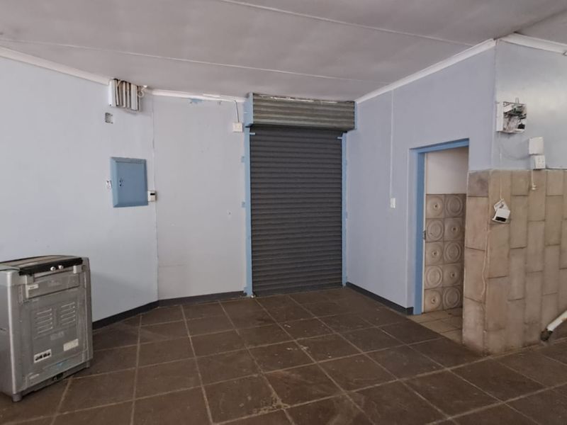 A functional utility or service area featuring a roller shutter door, tiled flooring, and a built-in sink with exposed plumbing connections.