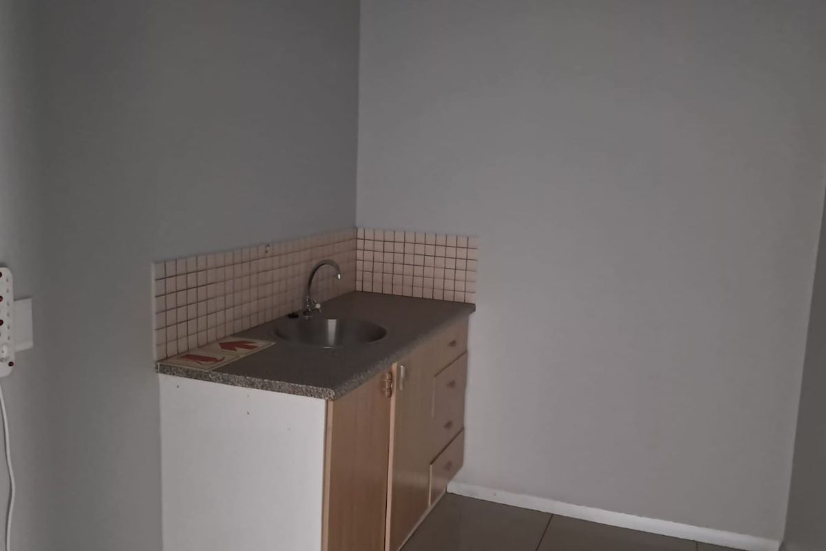 A compact office kitchenette featuring a small laminate countertop, integrated sink, and basic wooden cabinetry with a tiled splashback.