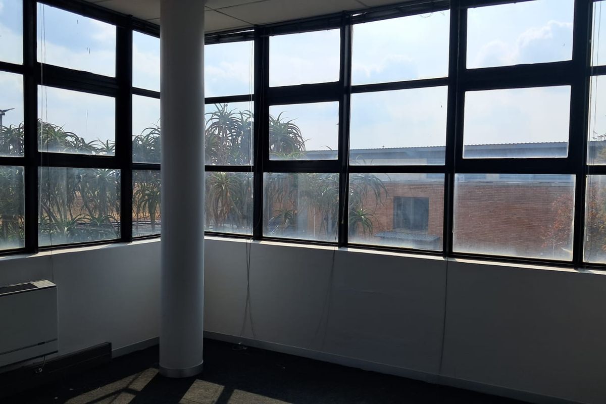 A bright, corner office space featuring expansive floor-to-ceiling windows, a central structural column, and integrated HVAC unit.