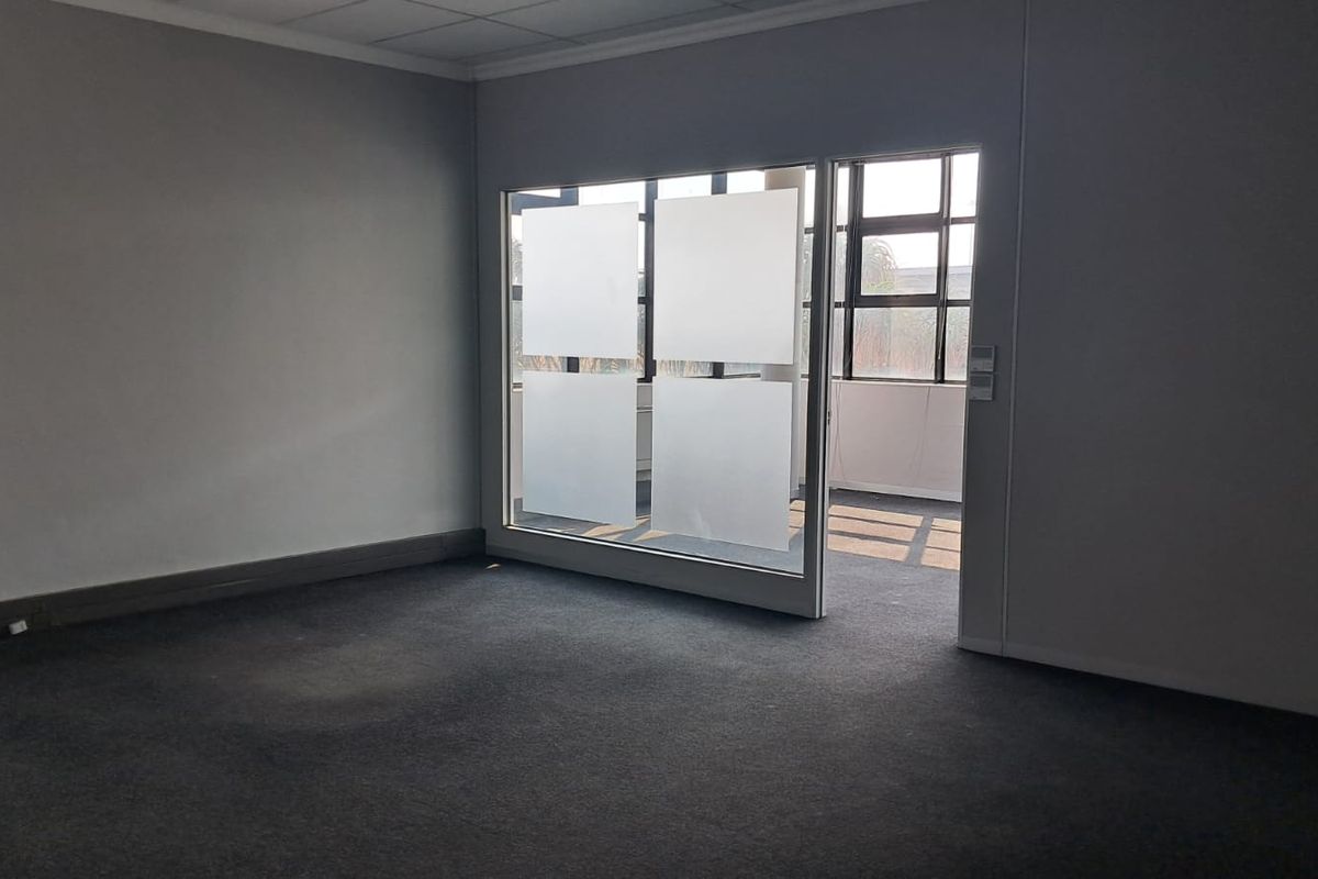 A vacant office space featuring grey carpeting, a suspended ceiling, and a glass partition with frosted privacy film.