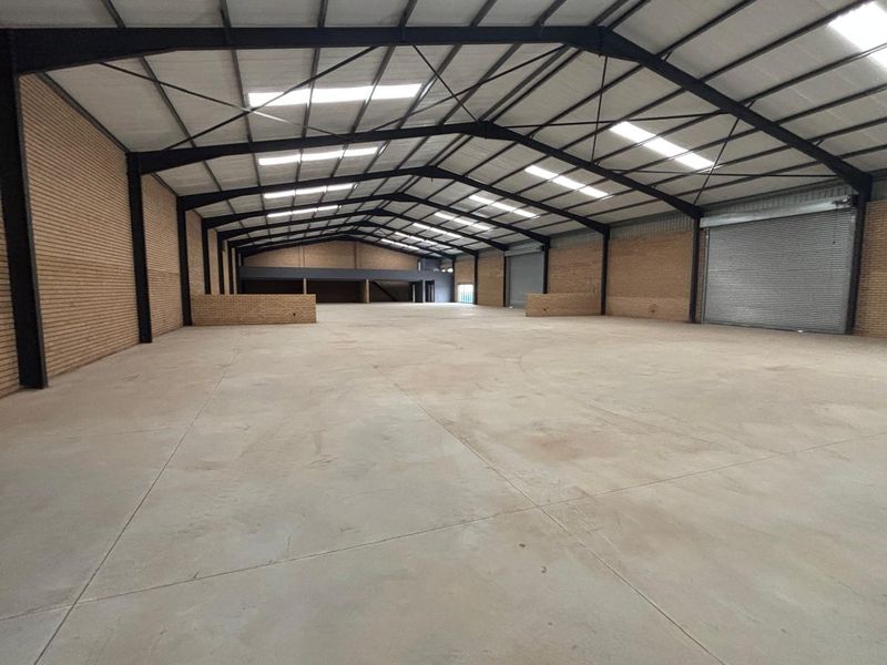 Spacious industrial warehouse featuring high ceilings, exposed steel portal frame, concrete flooring, face brick walls, and a large roller shutter door.