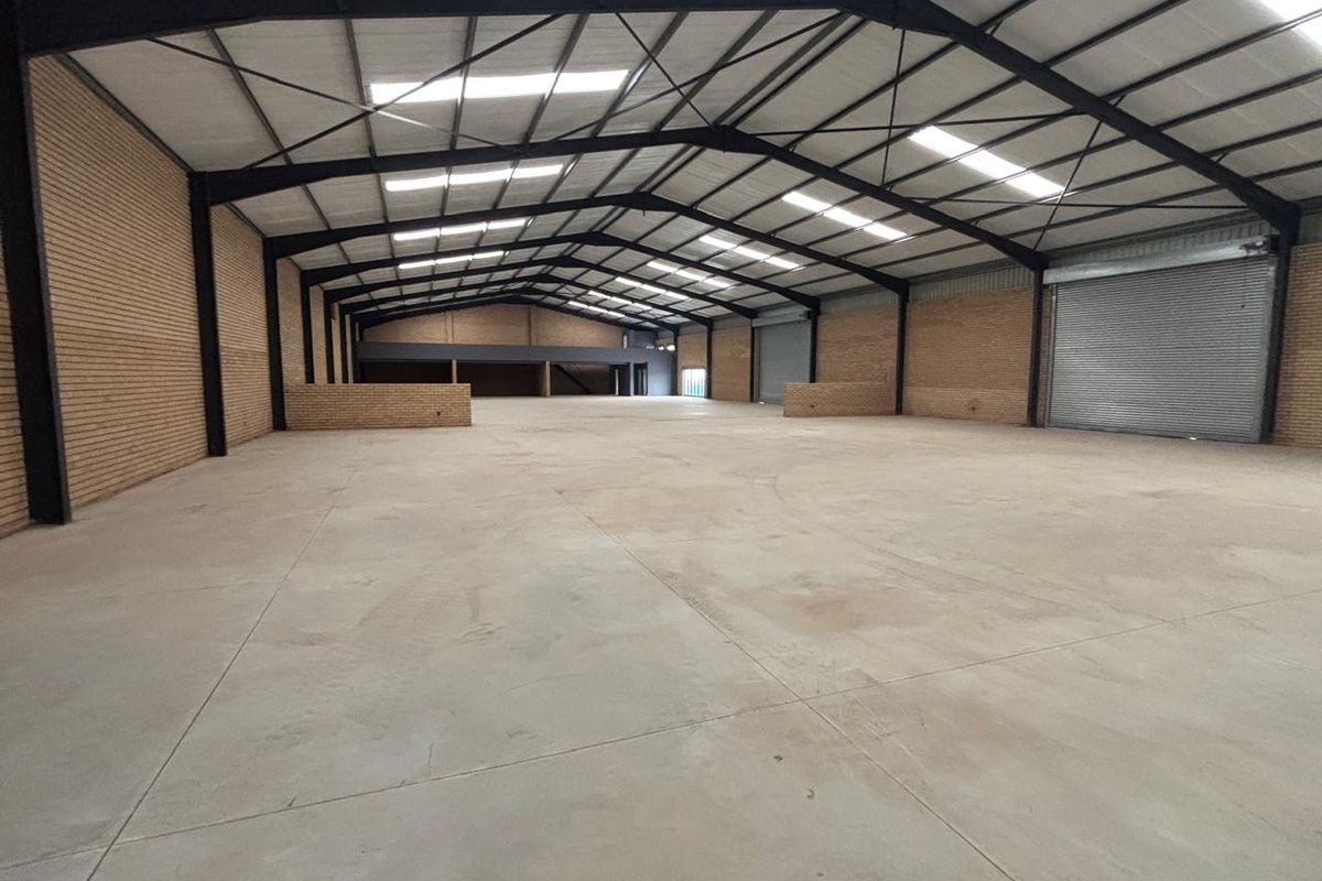 Spacious industrial warehouse featuring high ceilings, exposed steel portal frame, concrete flooring, face brick walls, and a large roller shutter door.