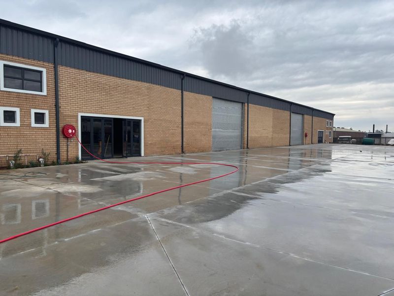 Industrial warehouse exterior featuring a large concrete yard, multiple roller shutter doors, and face brick facade with integrated fire safety equipment.