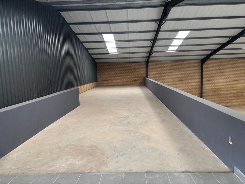 Spacious industrial mezzanine level featuring exposed steel trusses, corrugated metal cladding, face brick walls, and concrete flooring with integrated skylights.