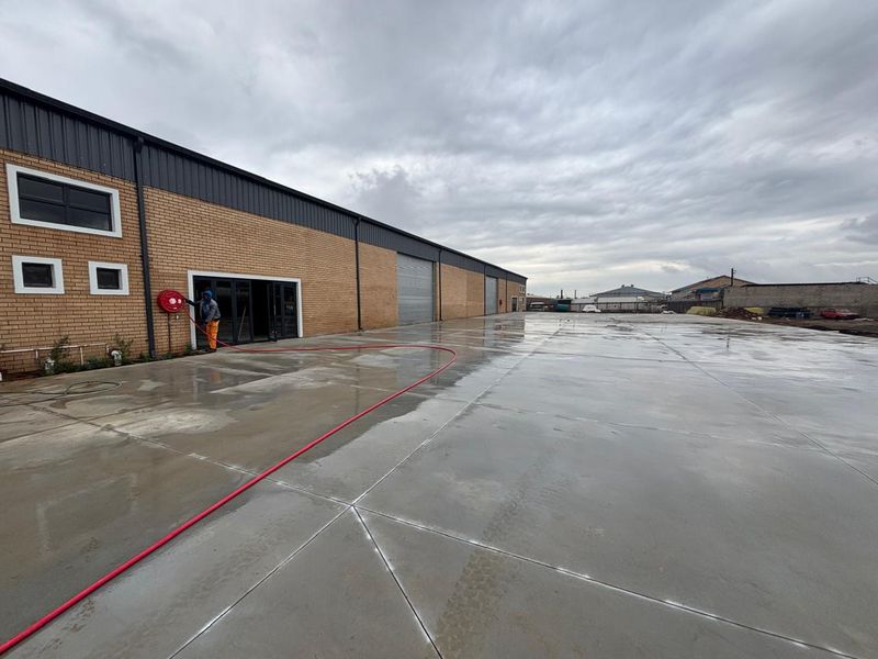 Spacious industrial rear yard featuring a large concrete surface, brick facade, and roller shutter access, suitable for logistics or storage operations.